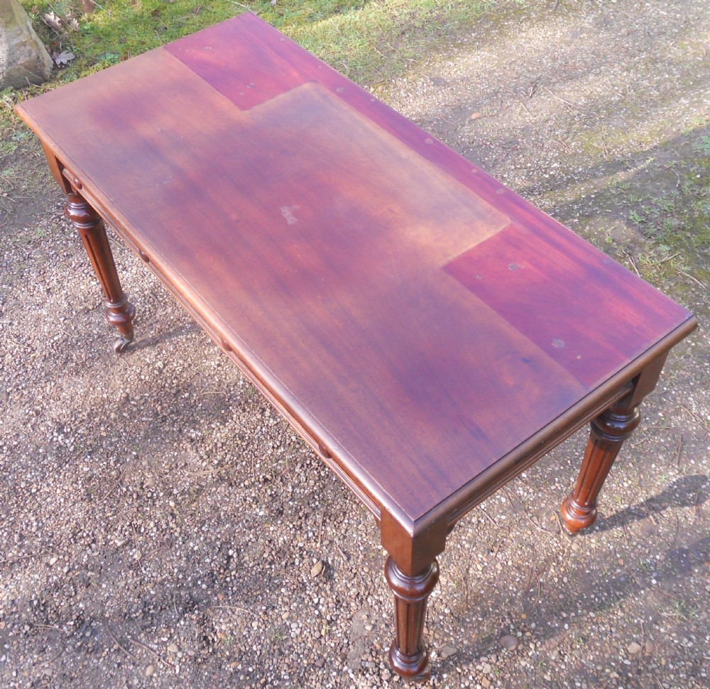 Victorian mahogany writing table featuring two frieze drawers with wooden knob handles, raised on turned and fluted legs with brass castors. View V