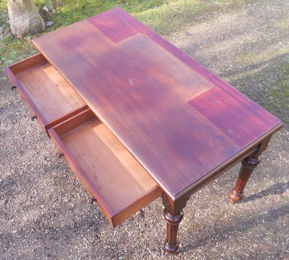 Victorian mahogany writing table featuring two frieze drawers with wooden knob handles, raised on turned and fluted legs with brass castors. View VI