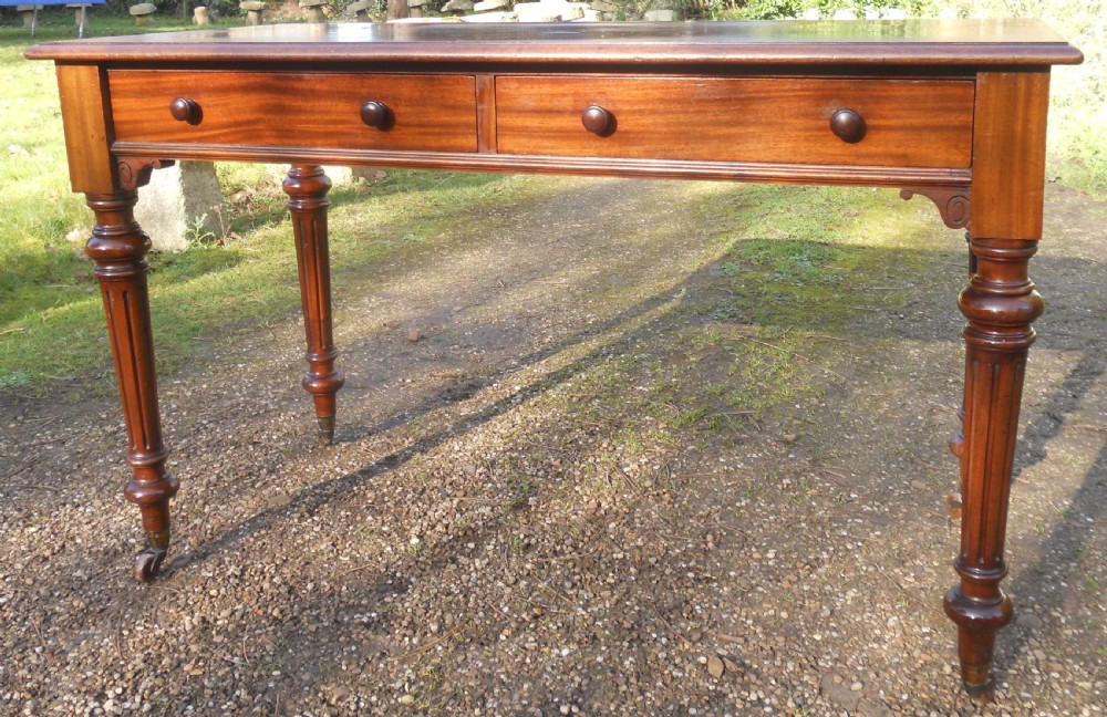 Victorian mahogany writing table featuring two frieze drawers with wooden knob handles, raised on turned and fluted legs with brass castors. View VII