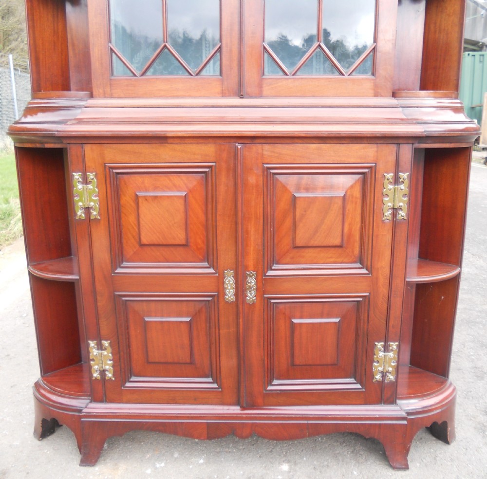 An Edwardian mahogany display cabinet featuring astragal glazed upper doors, lower panelled doors, open tiered side shelving, and decorative brass hardware. View V