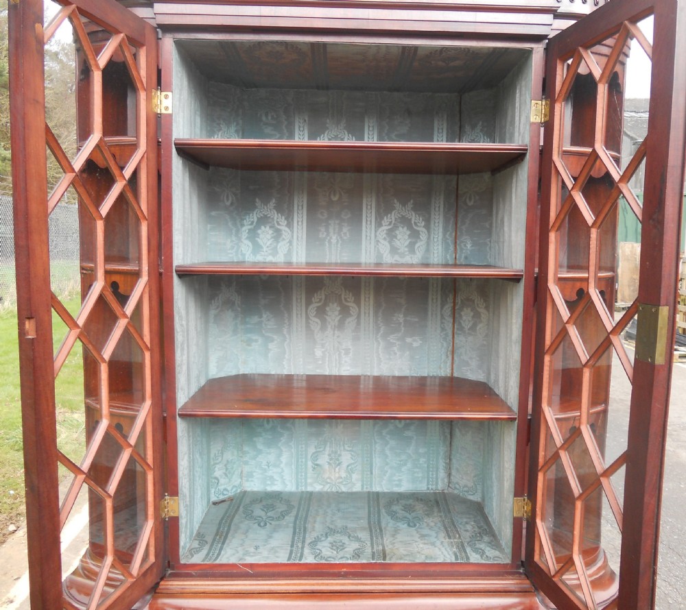 An Edwardian mahogany display cabinet featuring astragal glazed upper doors, lower panelled doors, open tiered side shelving, and decorative brass hardware. View IX