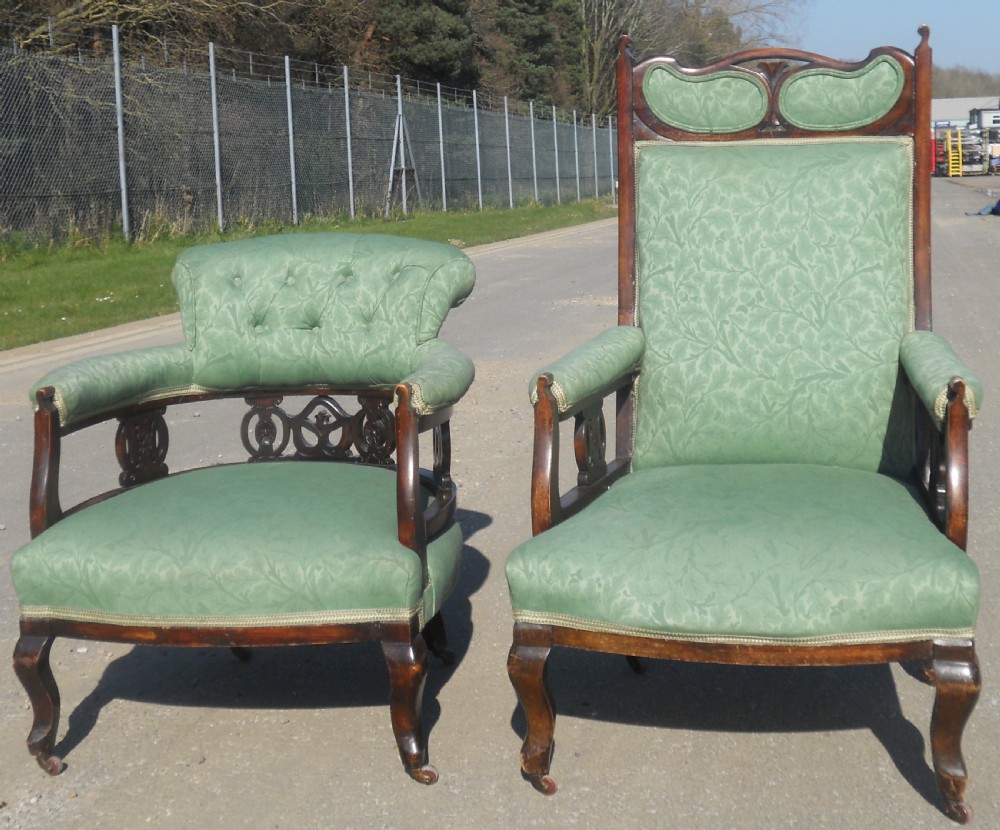 A pair of antique Art Nouveau mahogany armchairs upholstered in green patterned damask fabric with carved wooden frames and cabriole legs.
