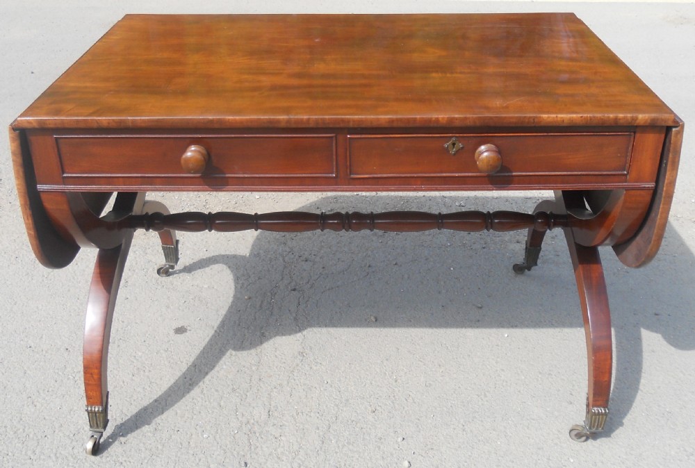 A Regency mahogany sofa table with two drop-leaf ends, twin drawers, turned stretchers, and curved sabre legs on brass castors.