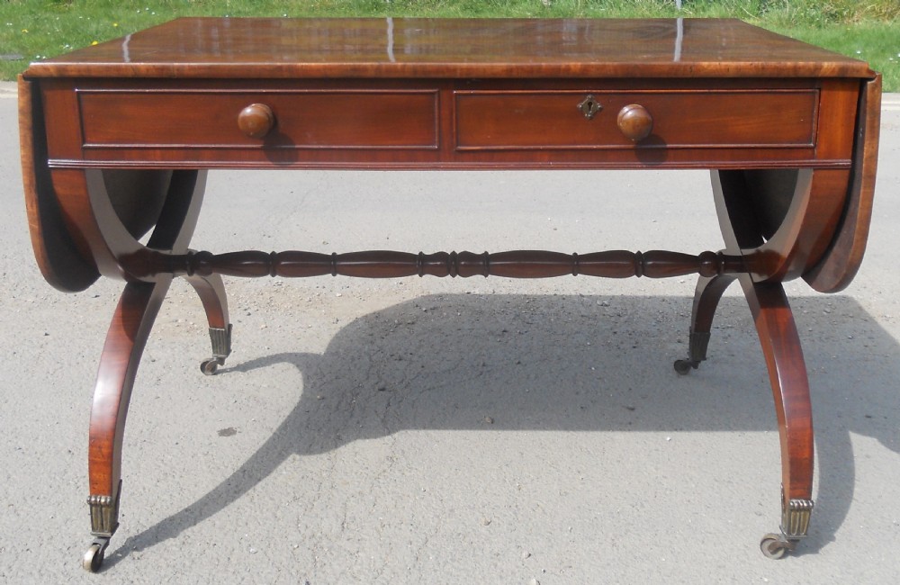 A Regency mahogany sofa table with two drop-leaf ends, twin drawers, turned stretchers, and curved sabre legs on brass castors. View II