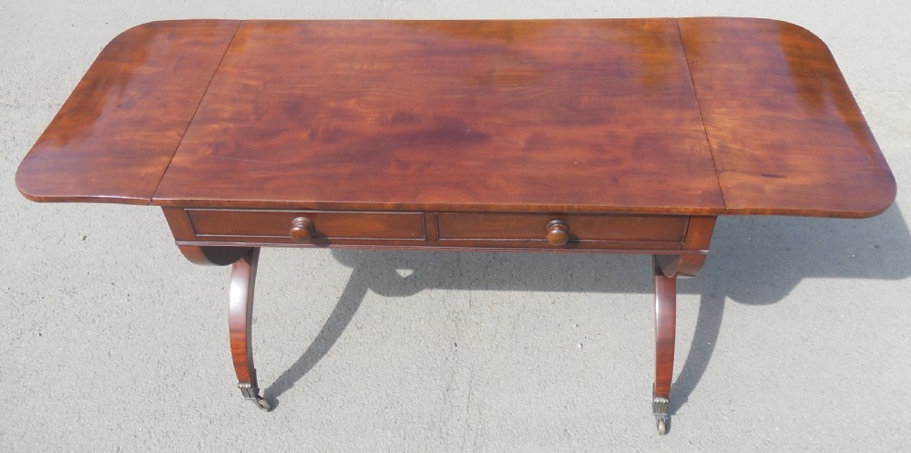 A Regency mahogany sofa table with two drop-leaf ends, twin drawers, turned stretchers, and curved sabre legs on brass castors. View V