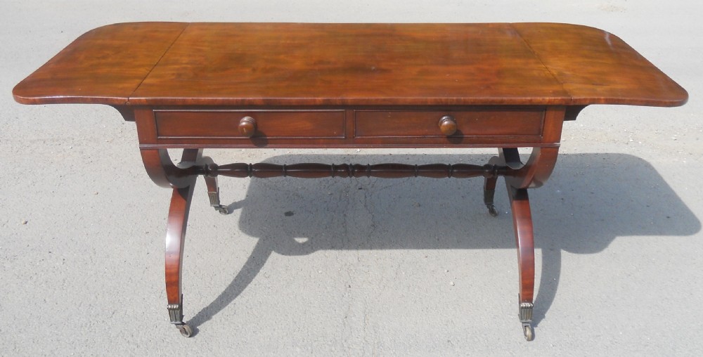 A Regency mahogany sofa table with two drop-leaf ends, twin drawers, turned stretchers, and curved sabre legs on brass castors. View VII