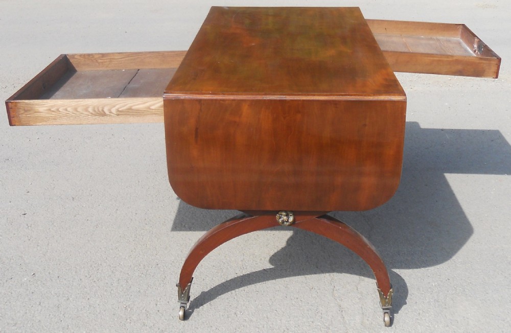 A Regency mahogany sofa table with two drop-leaf ends, twin drawers, turned stretchers, and curved sabre legs on brass castors. View XI