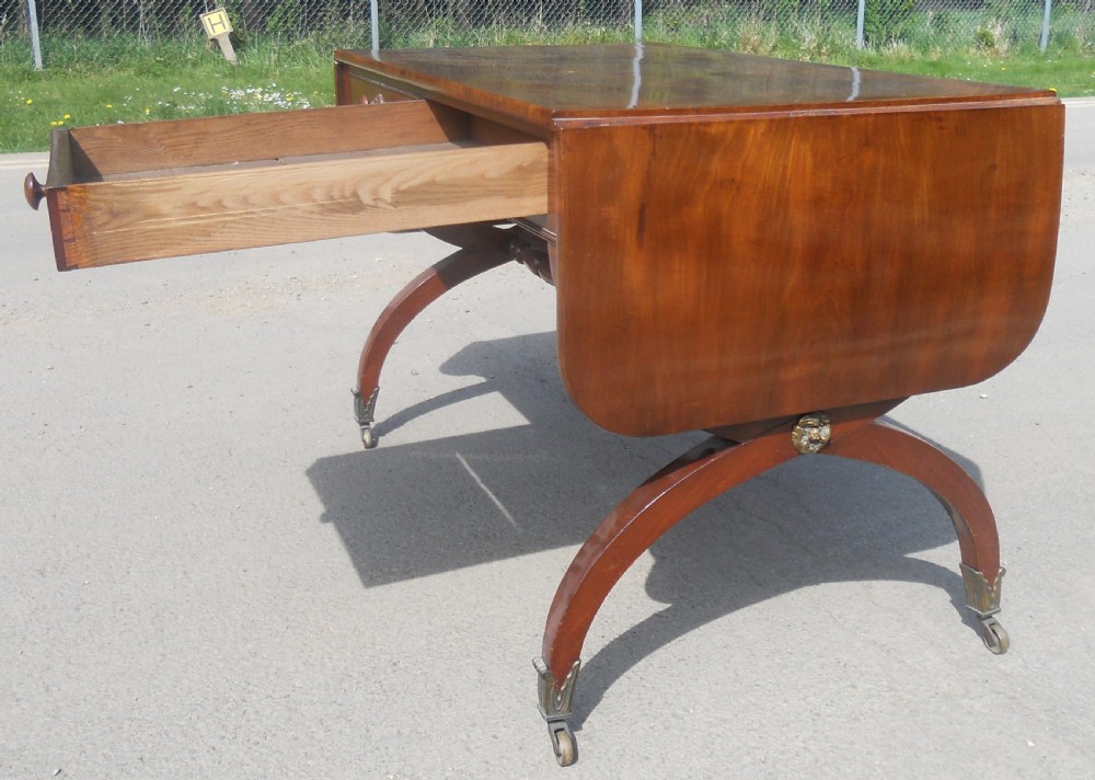 A Regency mahogany sofa table with two drop-leaf ends, twin drawers, turned stretchers, and curved sabre legs on brass castors. View XII