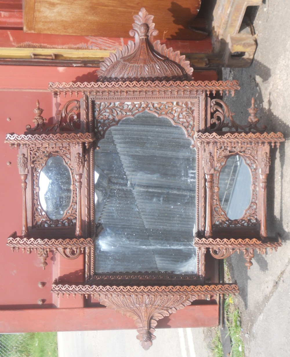 An intricately carved Victorian mahogany wall mirror featuring openwork fretwork, side display shelves with small mirror panels, an arched central mirror, and a carved top pediment. View II