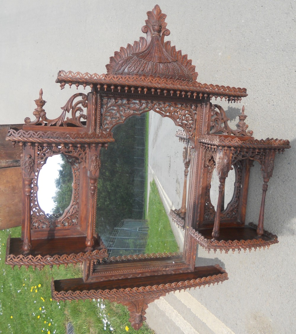 An intricately carved Victorian mahogany wall mirror featuring openwork fretwork, side display shelves with small mirror panels, an arched central mirror, and a carved top pediment. View III