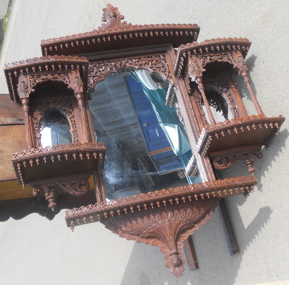 An intricately carved Victorian mahogany wall mirror featuring openwork fretwork, side display shelves with small mirror panels, an arched central mirror, and a carved top pediment. View IV