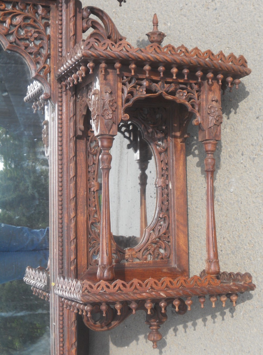 An intricately carved Victorian mahogany wall mirror featuring openwork fretwork, side display shelves with small mirror panels, an arched central mirror, and a carved top pediment. View V