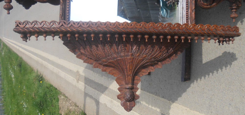 An intricately carved Victorian mahogany wall mirror featuring openwork fretwork, side display shelves with small mirror panels, an arched central mirror, and a carved top pediment. View VI