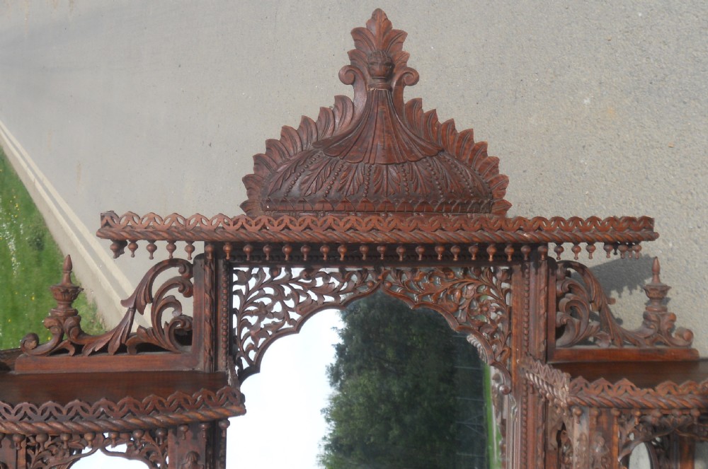 An intricately carved Victorian mahogany wall mirror featuring openwork fretwork, side display shelves with small mirror panels, an arched central mirror, and a carved top pediment. View VII