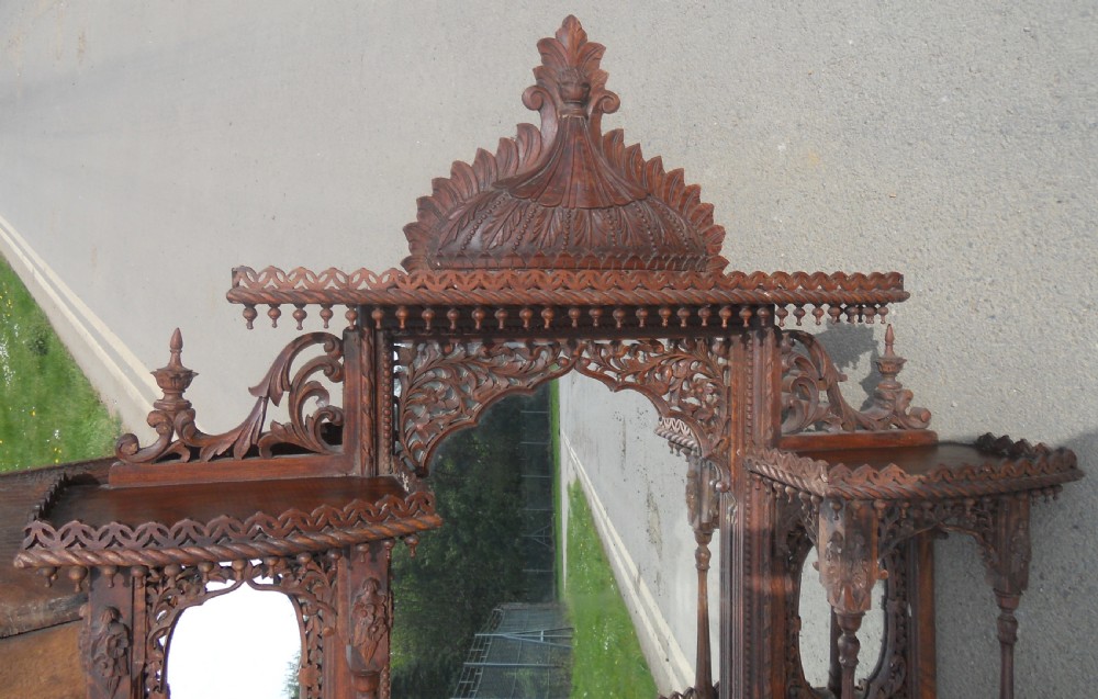 An intricately carved Victorian mahogany wall mirror featuring openwork fretwork, side display shelves with small mirror panels, an arched central mirror, and a carved top pediment. View IX