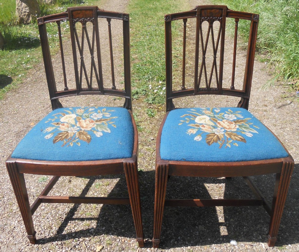A pair of Georgian mahogany dining chairs featuring carved lattice backrests and blue needlepoint seats embroidered with floral motifs.