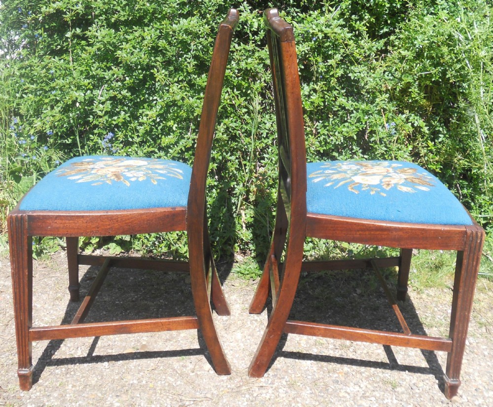 A pair of Georgian mahogany dining chairs featuring carved lattice backrests and blue needlepoint seats embroidered with floral motifs. View VI