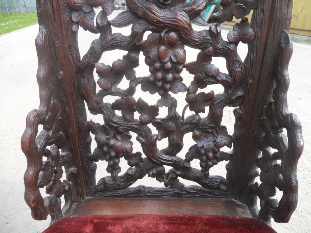 A dark carved oak prie-dieu prayer chair featuring intricate openwork grapevine back carvings with crimson velvet padded seat and top armrest. View V