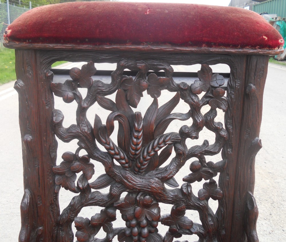 A dark carved oak prie-dieu prayer chair featuring intricate openwork grapevine back carvings with crimson velvet padded seat and top armrest. View VI