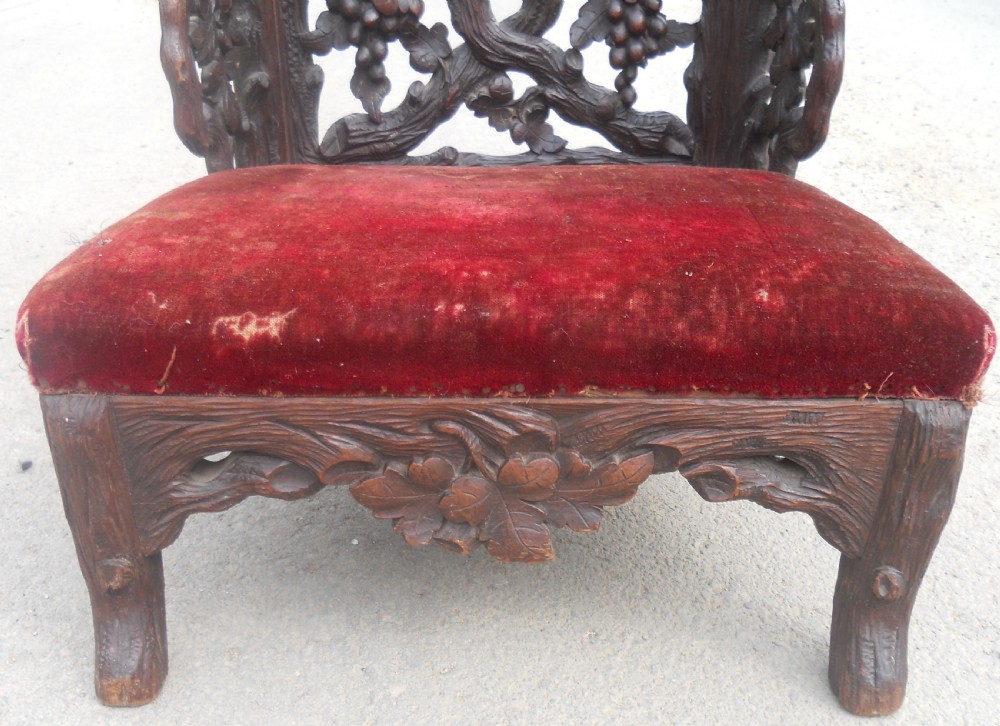 A dark carved oak prie-dieu prayer chair featuring intricate openwork grapevine back carvings with crimson velvet padded seat and top armrest. View VII