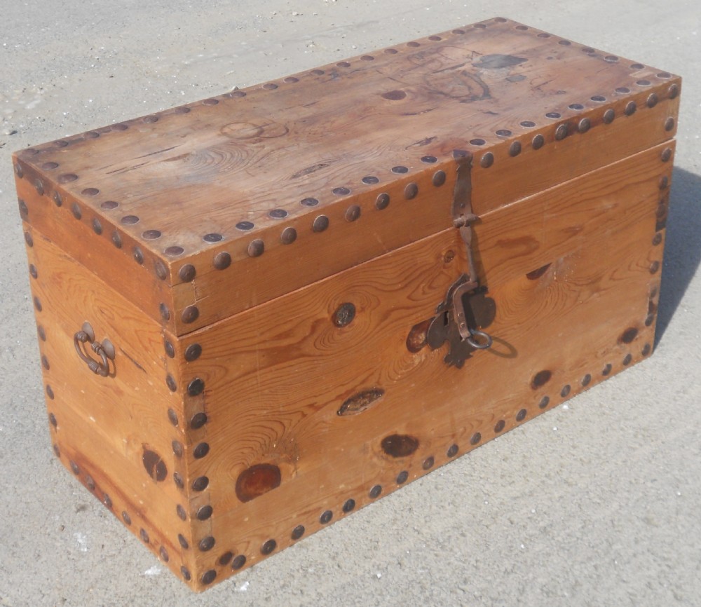 A rectangular Victorian pine wooden blanket box featuring studded iron trim along the edges, side drop handles, and an iron latch on the front.