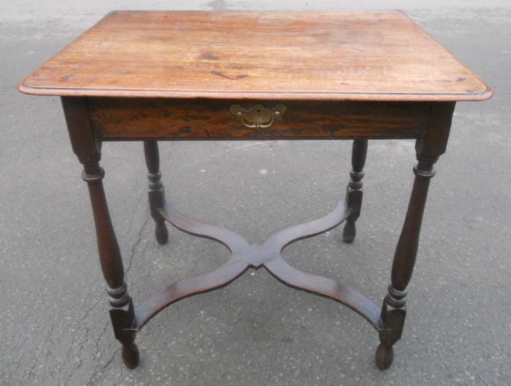 A Georgian oak side table featuring a rectangular top, a single drawer with a brass drop handle, turned legs, and a distinctive curved cross-stretcher base.