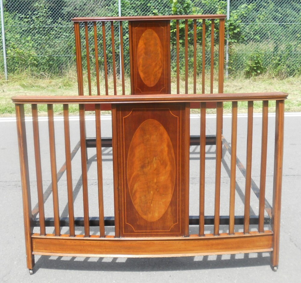 An Edwardian mahogany double bed frame featuring vertical slatted rails, central inlaid oval panels, and metal castors.