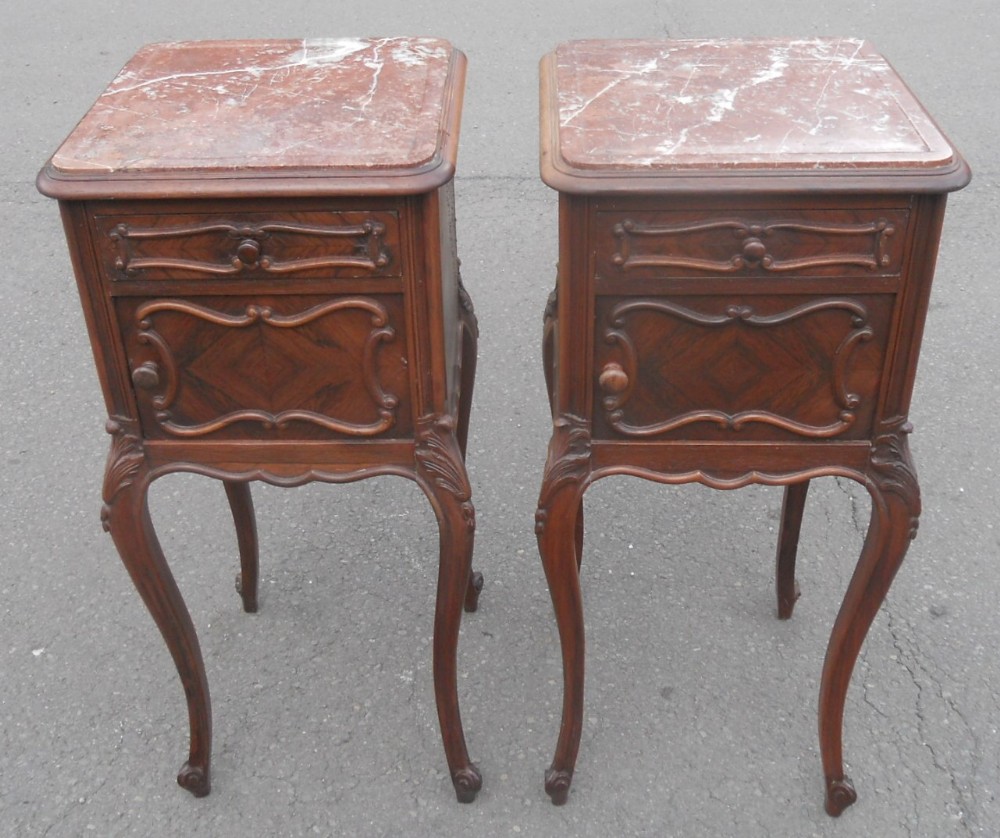 A pair of French style walnut bedside cabinets with reddish marble tops, carved single drawers, single cupboards, and slender cabriole legs.