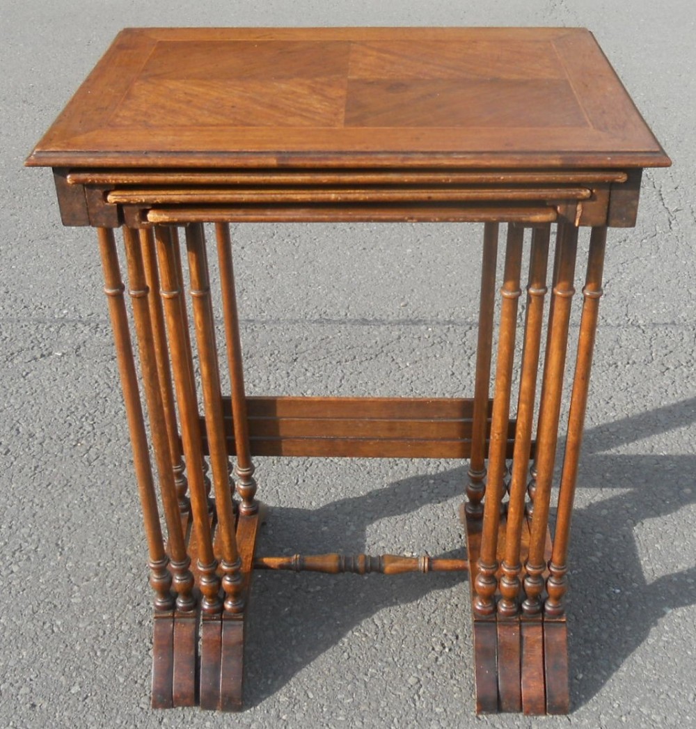 An Edwardian set of four nested walnut tables featuring quarter-veneered rectangular tops and slender turned spindle legs.
