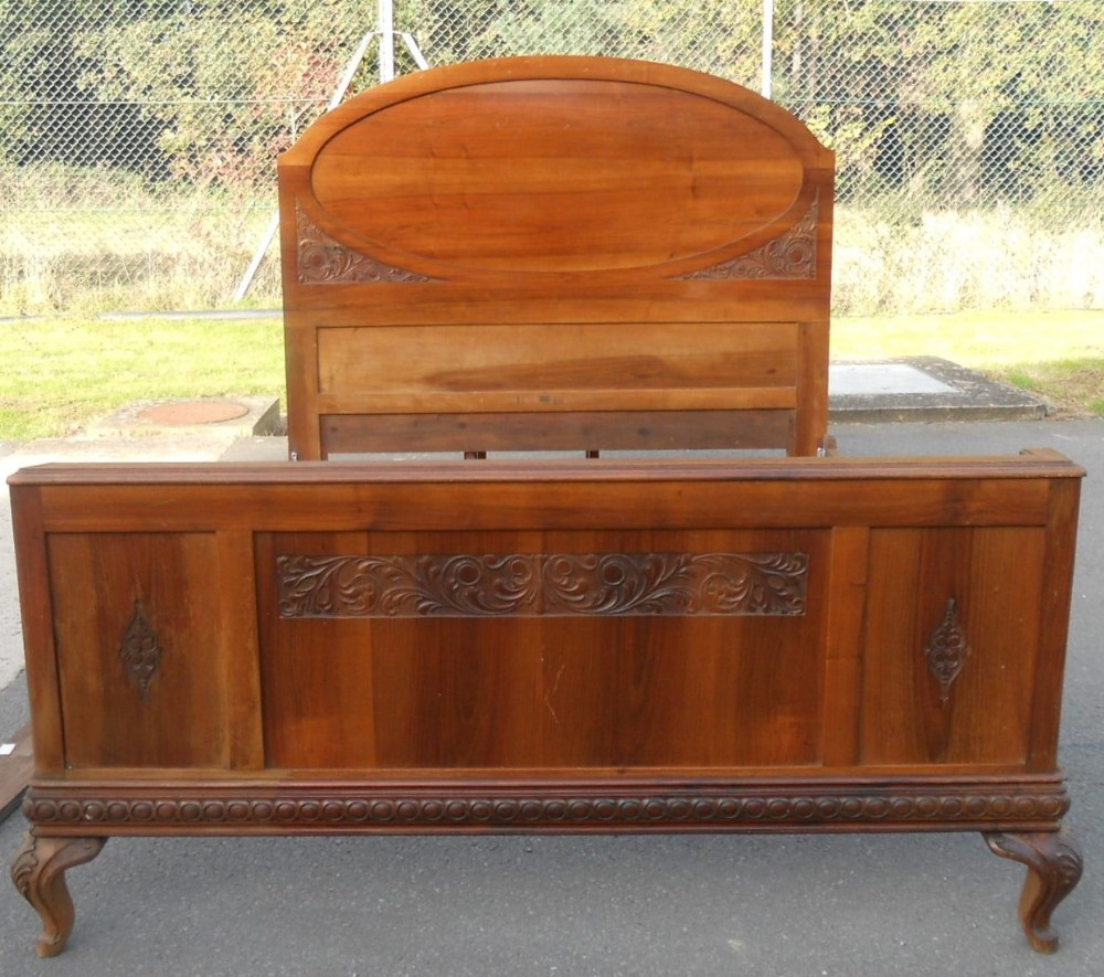 An antique Italian walnut double bed frame featuring a high headboard with an oval inset panel and a low footboard with carved details and cabriole legs.