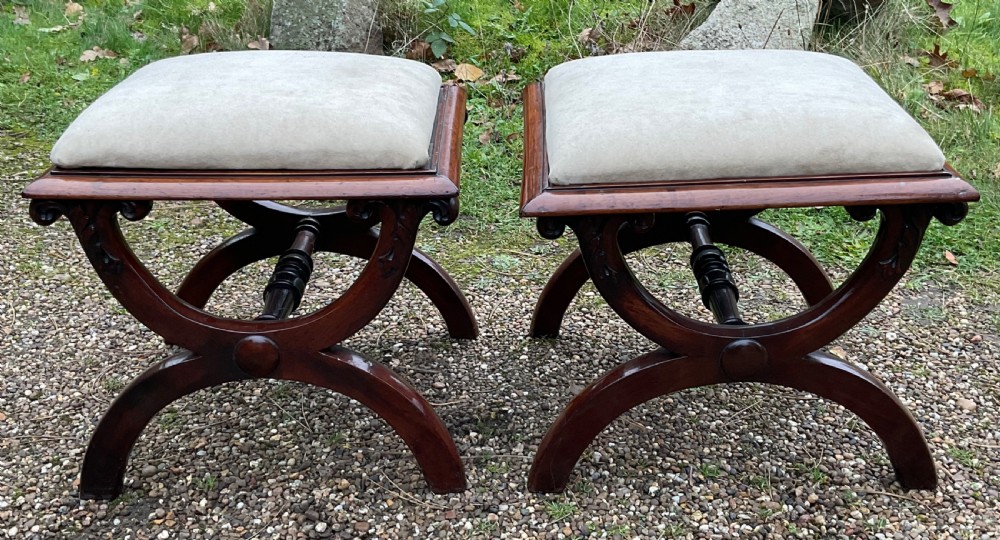A pair of William IV mahogany x-frame stools with neutral light beige upholstered padded tops and turned central stretchers.