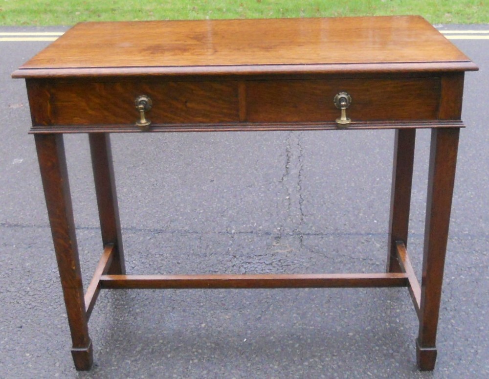 A rectangular Georgian style oak side table featuring drawers with brass drop handles and straight legs connected by stretchers.