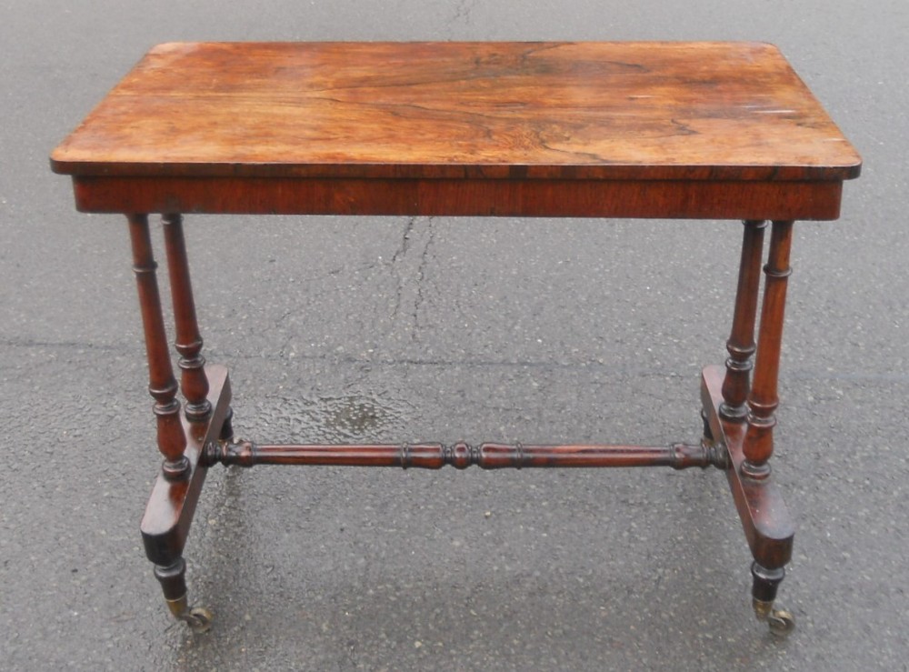 A Victorian rosewood centre table featuring a rectangular figured top, twin turned end supports, a central turned stretcher, and brass castors.
