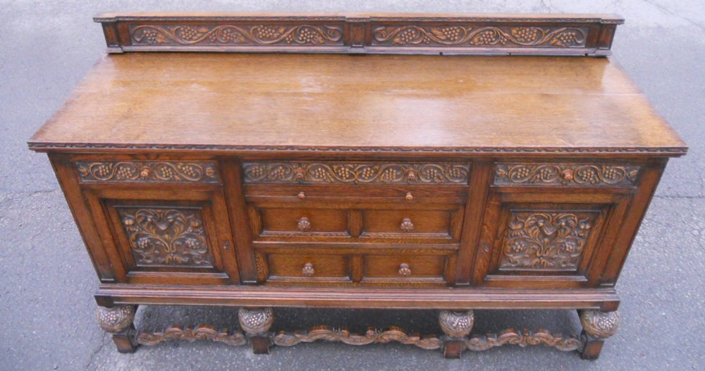 A large carved oak sideboard featuring a low gallery back, central drawers, flanking cupboard doors with foliate carvings, and carved bulbous feet.