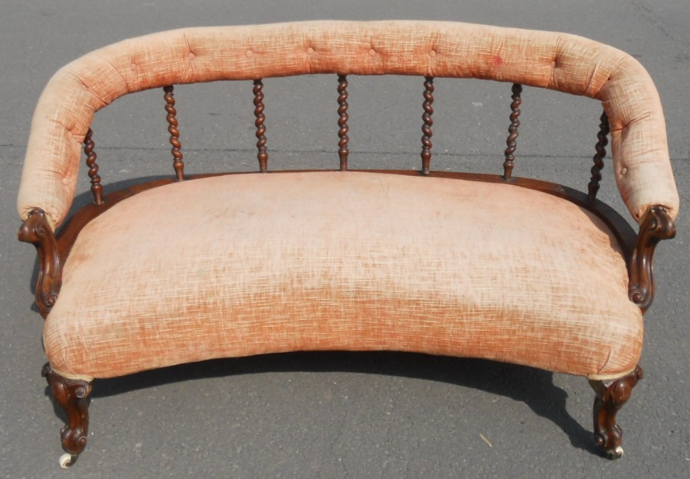 A Victorian salon settee featuring a curved peach-upholstered padded backrest supported by dark wood barley twist spindles, a wide cushioned seat, and carved front legs on castors.