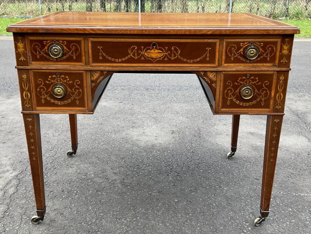 An Edwardian mahogany writing desk featuring urn and floral marquetry inlays, five drawers with circular brass pulls, tapered legs, and brass castors. View II
