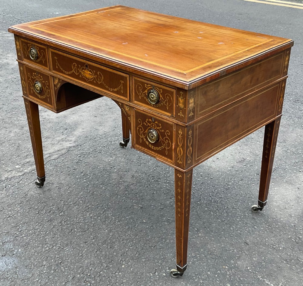 An Edwardian mahogany writing desk featuring urn and floral marquetry inlays, five drawers with circular brass pulls, tapered legs, and brass castors. View III