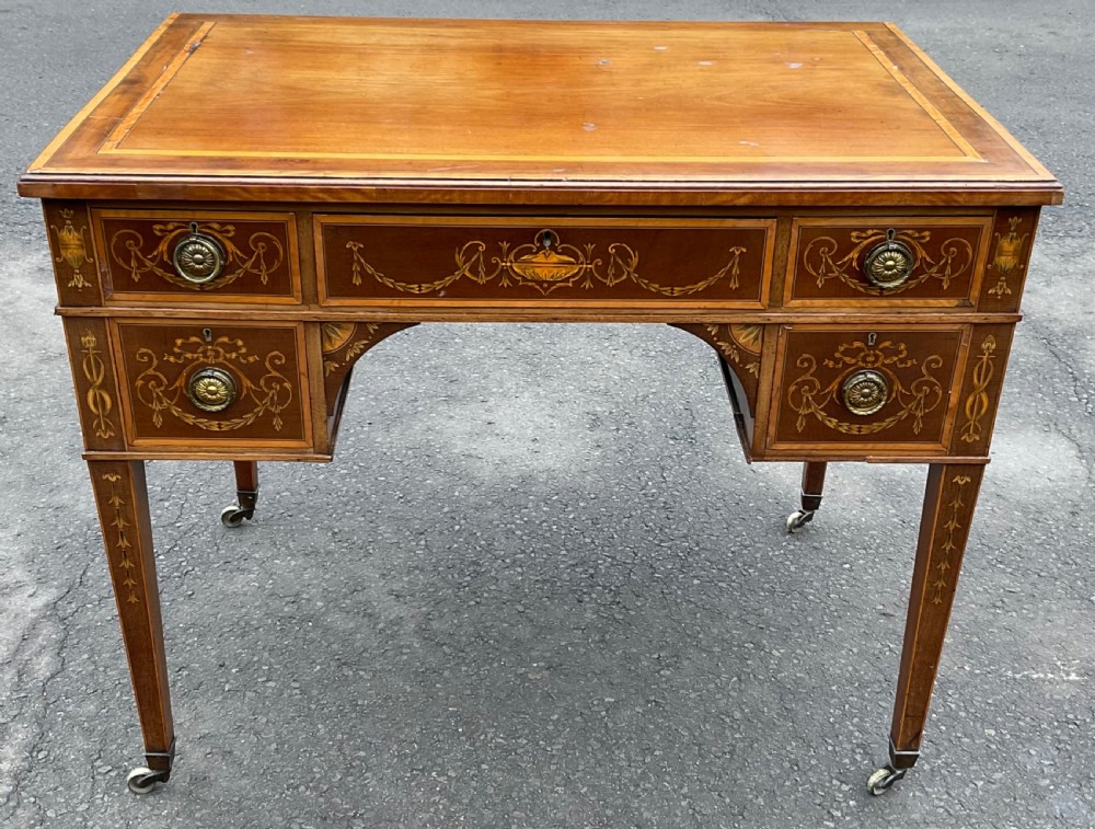 An Edwardian mahogany writing desk featuring urn and floral marquetry inlays, five drawers with circular brass pulls, tapered legs, and brass castors. View IX