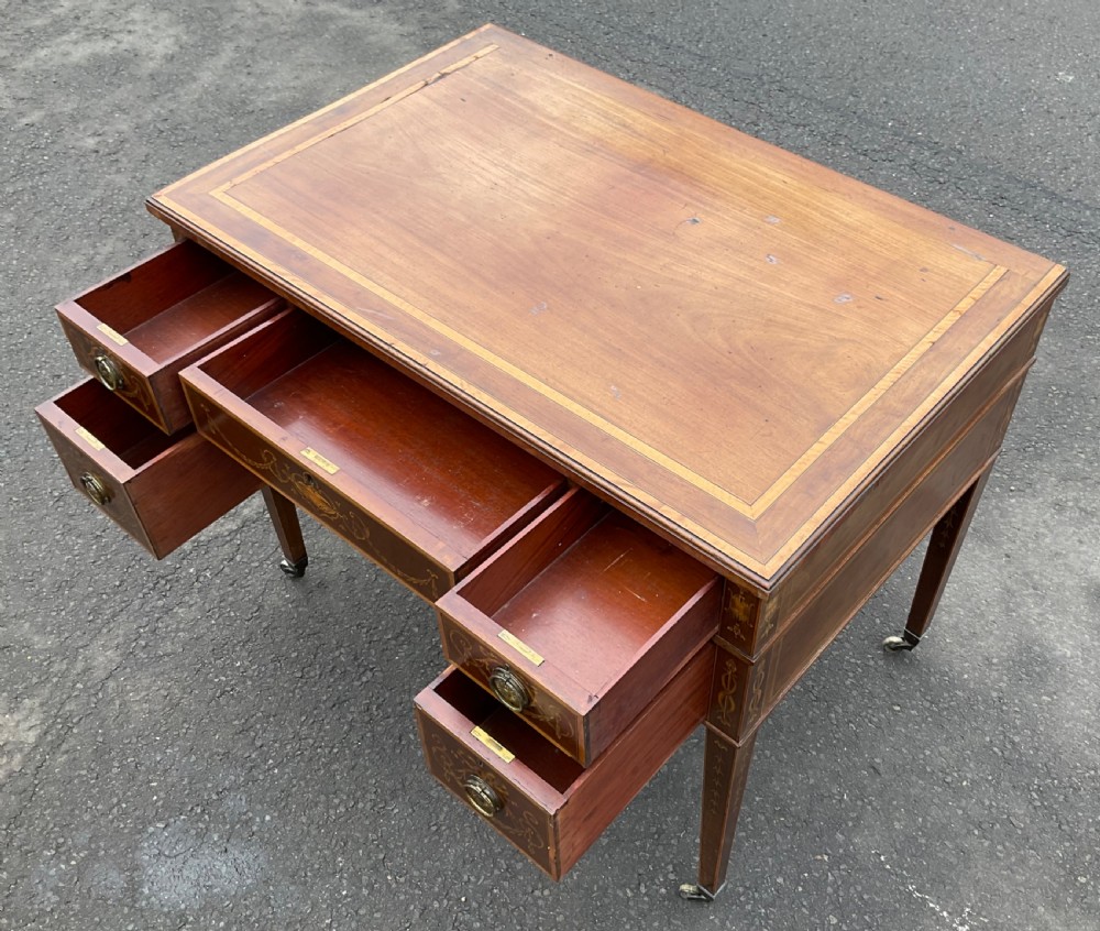 An Edwardian mahogany writing desk featuring urn and floral marquetry inlays, five drawers with circular brass pulls, tapered legs, and brass castors. View XI