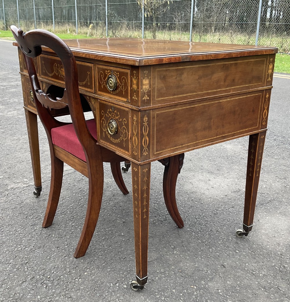 An Edwardian mahogany writing desk featuring urn and floral marquetry inlays, five drawers with circular brass pulls, tapered legs, and brass castors. View XII