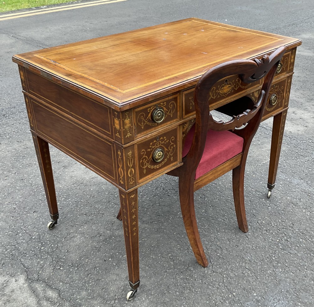 An Edwardian mahogany writing desk featuring urn and floral marquetry inlays, five drawers with circular brass pulls, tapered legs, and brass castors. View XIII