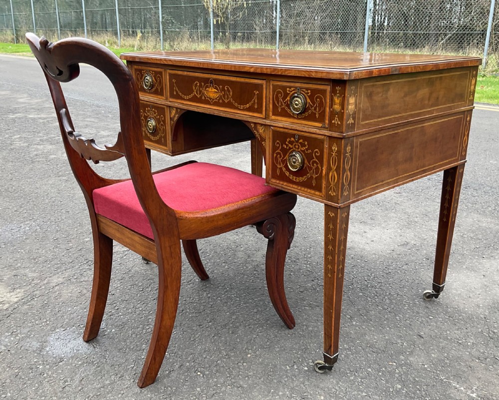 An Edwardian mahogany writing desk featuring urn and floral marquetry inlays, five drawers with circular brass pulls, tapered legs, and brass castors. View XIV