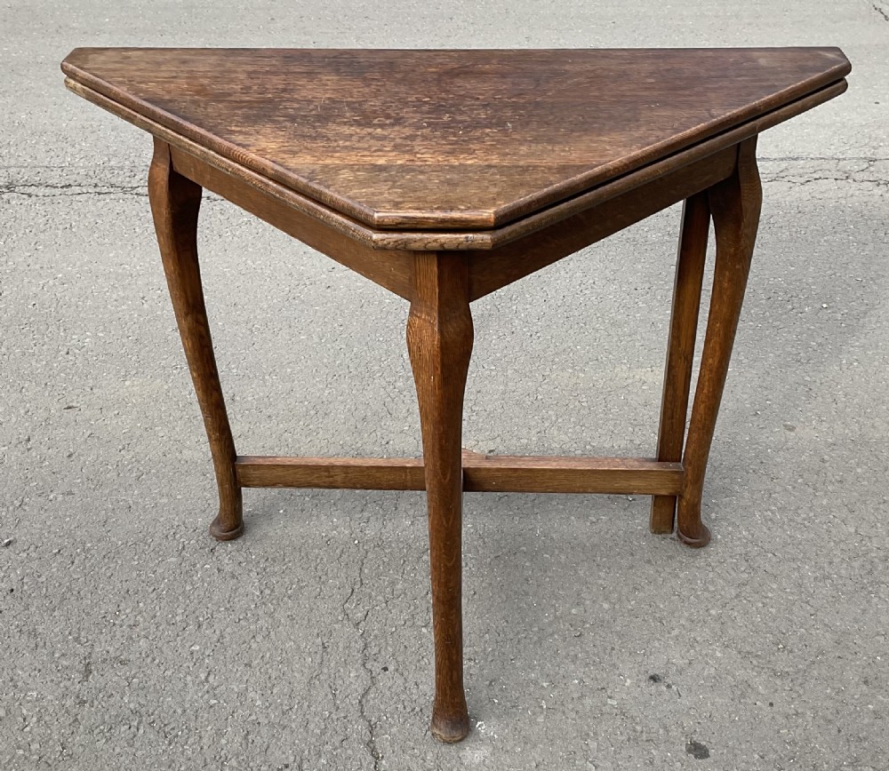 Triangular solid oak folding card table with three shaped legs and lower support stretchers.