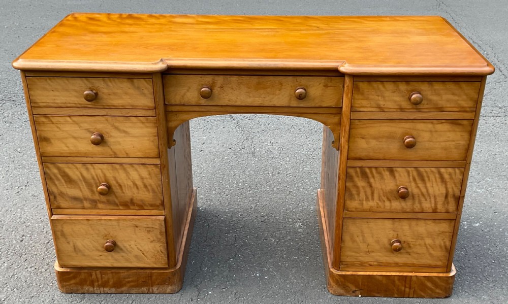 A Victorian satin birch twin-pedestal writing desk featuring nine drawers with turned timber knobs, a central arched kneehole, and plinth bases.