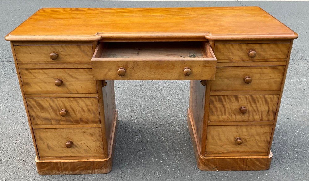 A Victorian satin birch twin-pedestal writing desk featuring nine drawers with turned timber knobs, a central arched kneehole, and plinth bases. View IV