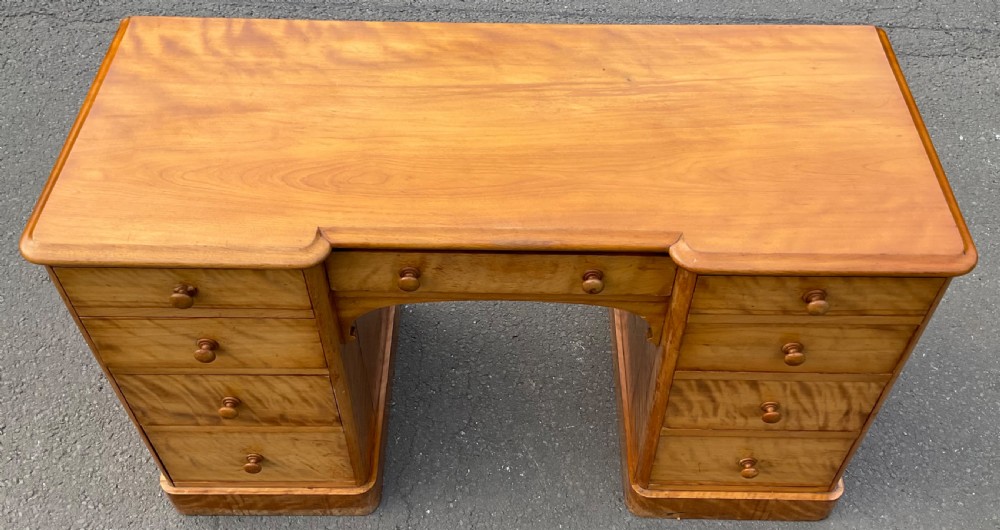 A Victorian satin birch twin-pedestal writing desk featuring nine drawers with turned timber knobs, a central arched kneehole, and plinth bases. View V