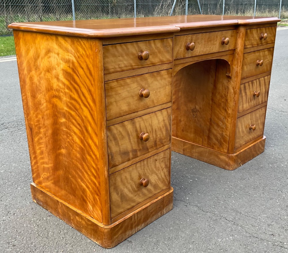 A Victorian satin birch twin-pedestal writing desk featuring nine drawers with turned timber knobs, a central arched kneehole, and plinth bases. View VI