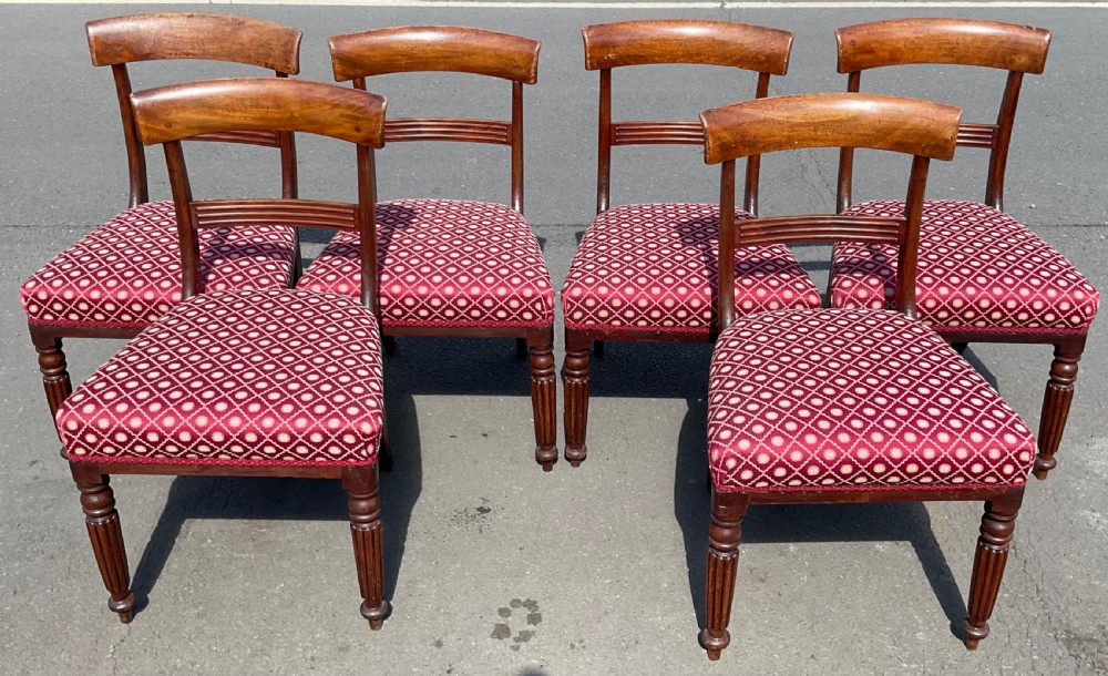 A set of six Victorian mahogany dining chairs featuring curved top rails, horizontal back slats, fluted front legs, and red patterned upholstered seats.