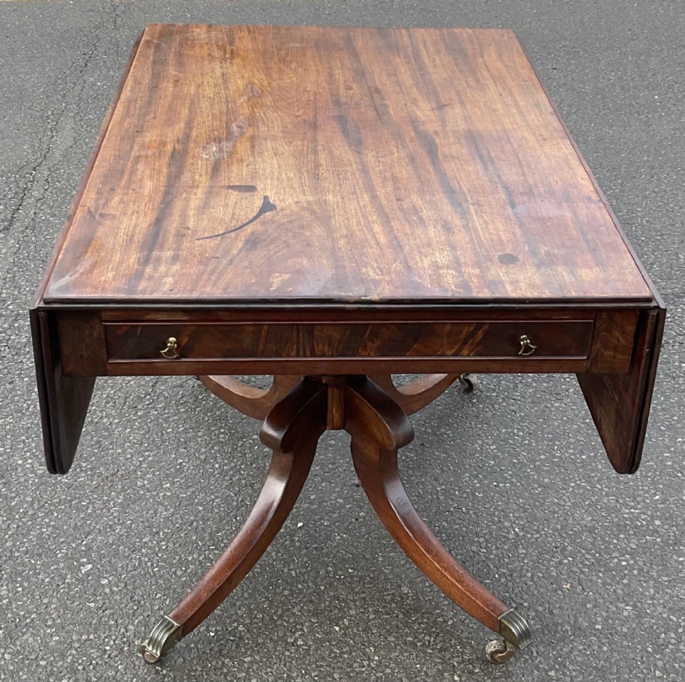 A Georgian mahogany drop-leaf table featuring a rectangular top, a frieze drawer with brass handles, and a four-legged pedestal base with brass castors.
