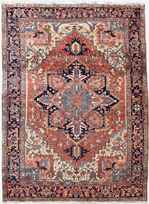 An antique Persian Heriz wool carpet with a large central geometric medallion in terracotta, navy blue, and light blue against an ivory and red field. View II